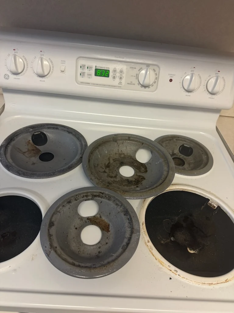 Electric stovetop with burnt-on grease on the drip pans before cleaning by Spotless Cleaning Services in Monroe, NC